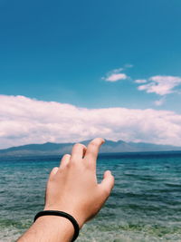 Cropped hand of person pointing against sea and sky