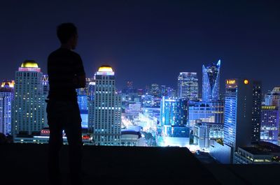 Rear view of silhouette mid adult man looking at illuminated cityscape during night