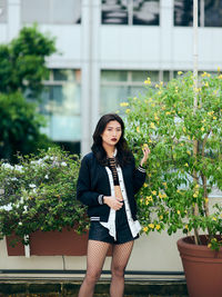 Portrait of young woman standing by potted plant