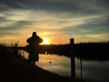 Silhouette man standing by lake against sky during sunset