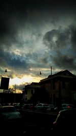 Cars on road by buildings against sky at sunset