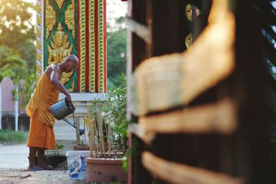 Side view of monk watering plants at temple