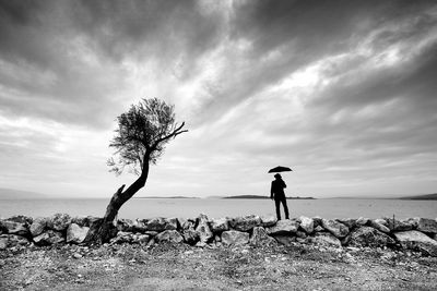 Man standing on rock by sea against sky