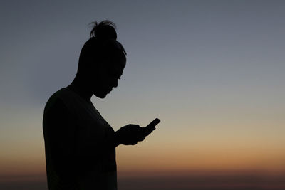 Silhouette woman using mobile phone against sky during sunset