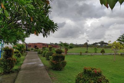 Footpath in park against cloudy sky