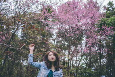 Portrait of beautiful young woman standing by flower tree