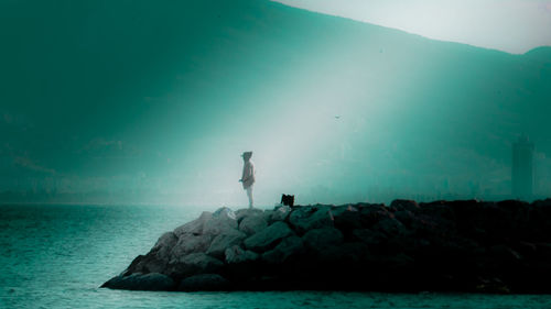 Man standing on rock by sea against sky