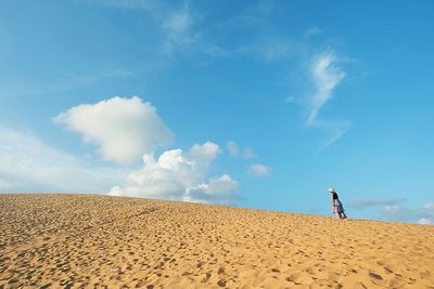 Woman on sand dune at beach against blue sky
