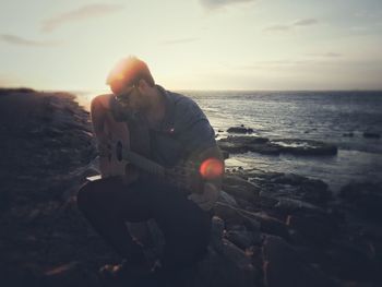 Man photographing sea against sky during sunset