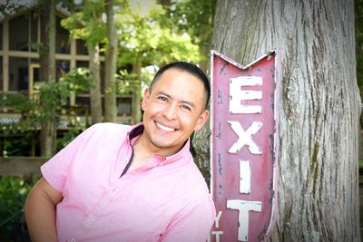 Portrait of smiling man leaning against exit sign on tree