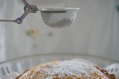 Close-up of strainer over cake with powdered sugar on cakestand