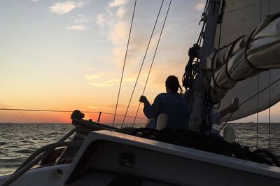 People sitting on sailboat by sea against sky during sunset