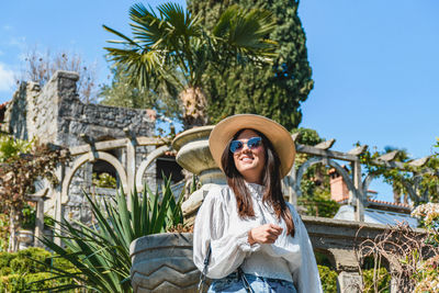 Front view of attractive young woman in spring outfit standing in beautiful park.