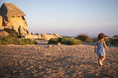 Rear view of baby girl standing on rock against sky