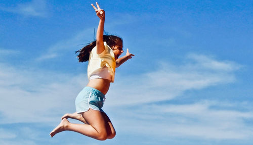 Low angle view of woman jumping against sky