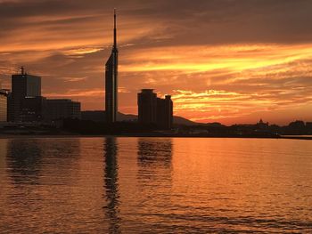 Silhouette buildings by river against orange sky