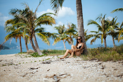 Young woman relaxing by palm tree at beach