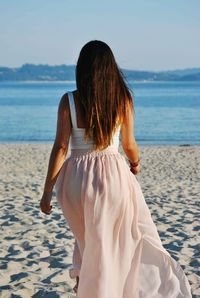 Rear view of woman walking on sand at beach against sky