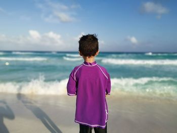 Rear view of kid standing on beach against sky