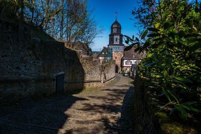 Footpath amidst trees and buildings against sky