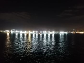 Illuminated city by sea against sky at night