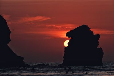 Silhouette rock formation in sea against sky during sunset