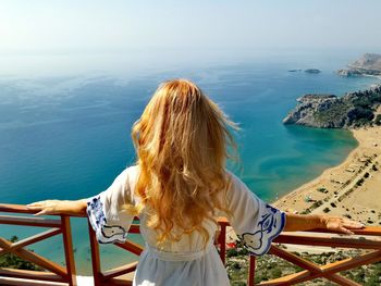 Rear view of woman with blond hair looking at sea during sunny day