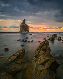 Rocks on beach against sky during sunset