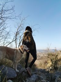 Young woman with dog standing on landscape against clear sky