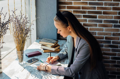 A young woman is sitting at a table and writing in a notebook.a business woman works as a freelancer