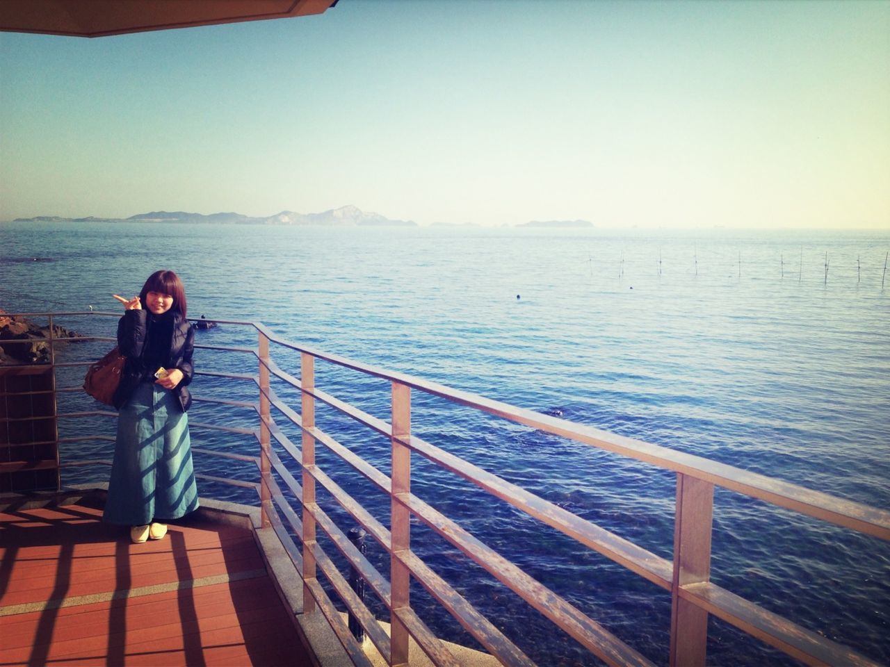 sea, water, railing, lifestyles, standing, clear sky, leisure activity, copy space, rear view, full length, scenics, pier, tranquil scene, horizon over water, tranquility, casual clothing, looking at view, beauty in nature