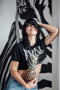 Portrait of smiling young woman with pineapple standing against wall