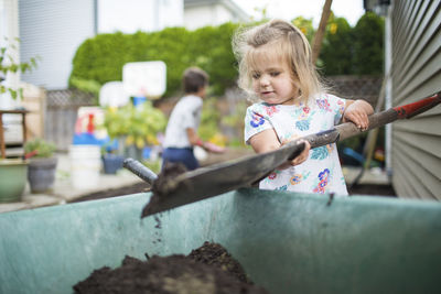 Cute girl shoveling dirt into wheelbarrow in backyard.