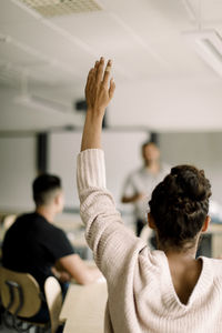 Female student with hand raised while tutor standing in classroom