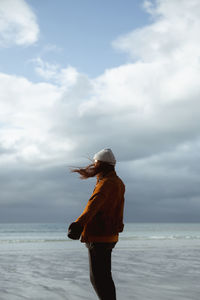 Rear view of woman standing at beach against sky