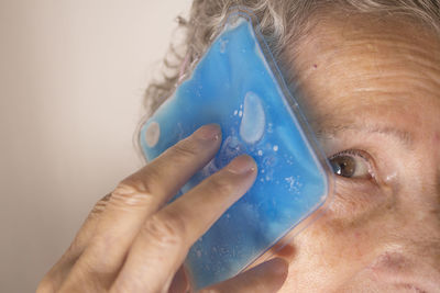 Close-up of woman holding ice pack to forehead against brown background