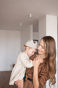 Mother dances cuddling her baby girl on hands in new empty home.