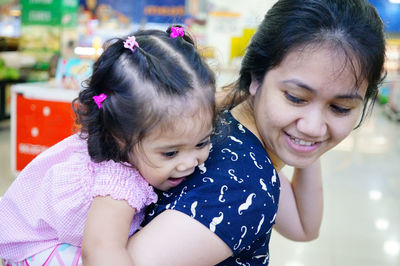 Smiling mother carrying daughter in supermarket