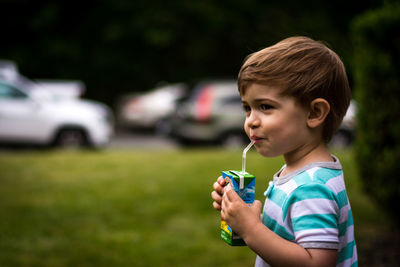 Side view of boy having drink while standing on field