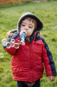 Boy in warm clothing blowing bubbles on field