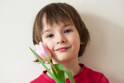Portrait of a smiling girl with freckles in a red t-shirt with a pink tulip on a white background