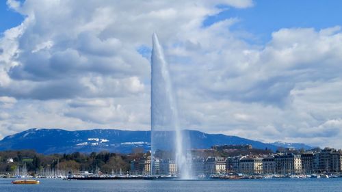 Fountain in city against cloudy sky