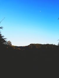 Silhouette trees on landscape against clear blue sky