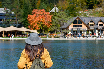 Rear view of woman standing on shore of lake, looking at beautiful tourist resort