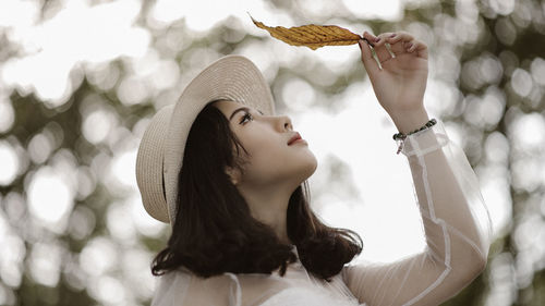 Close-up of young woman looking at leaf against trees