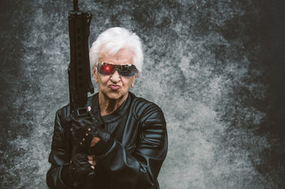 Portrait of senior woman holding rifle against wall