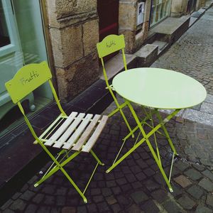 High angle view of empty chairs and table on sidewalk against building