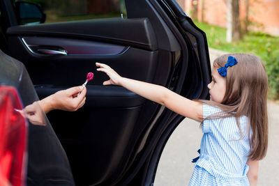 Cropped hand of person in car giving lollipop to girl on road