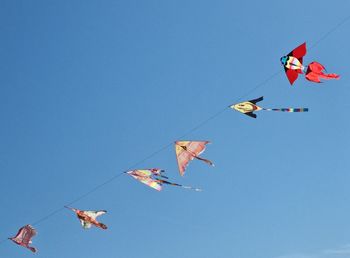 Low angle view of kites flying against clear blue sky