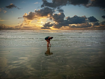 Full length of woman standing on beach against sky during sunset